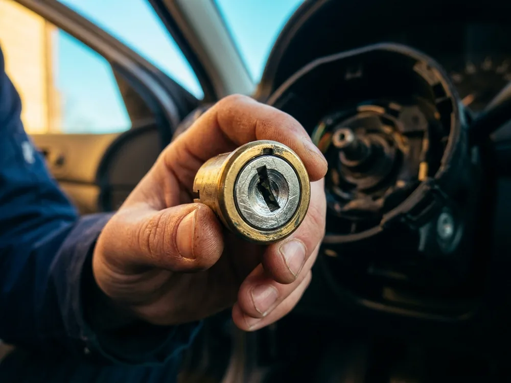 Ignition lock cylinder held in hand just after removal from an opened steering column