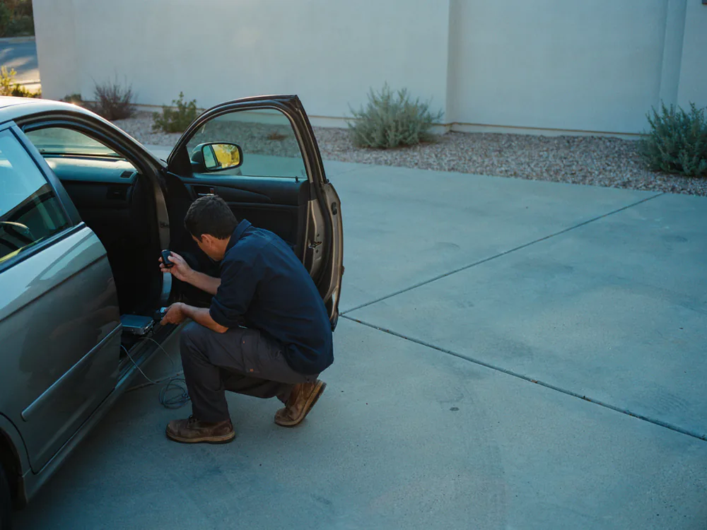 Key fob being programmed at the open driver door of a car in a residential driveway