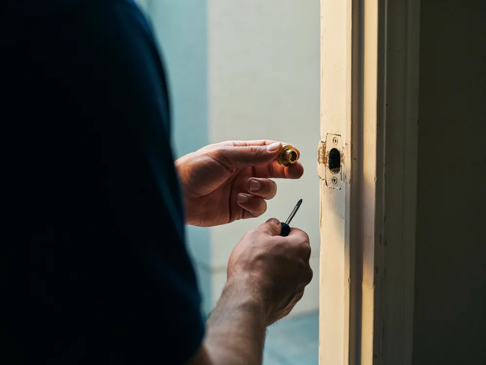 Brass deadbolt cylinder removed from a front door during a rekey, the empty lock bore visible in the door edge