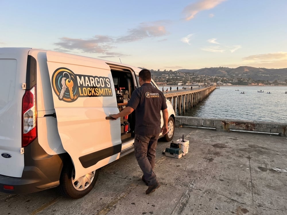 Marco's Locksmith service van parked by the water at dusk, side door open and a technician at the equipment racks